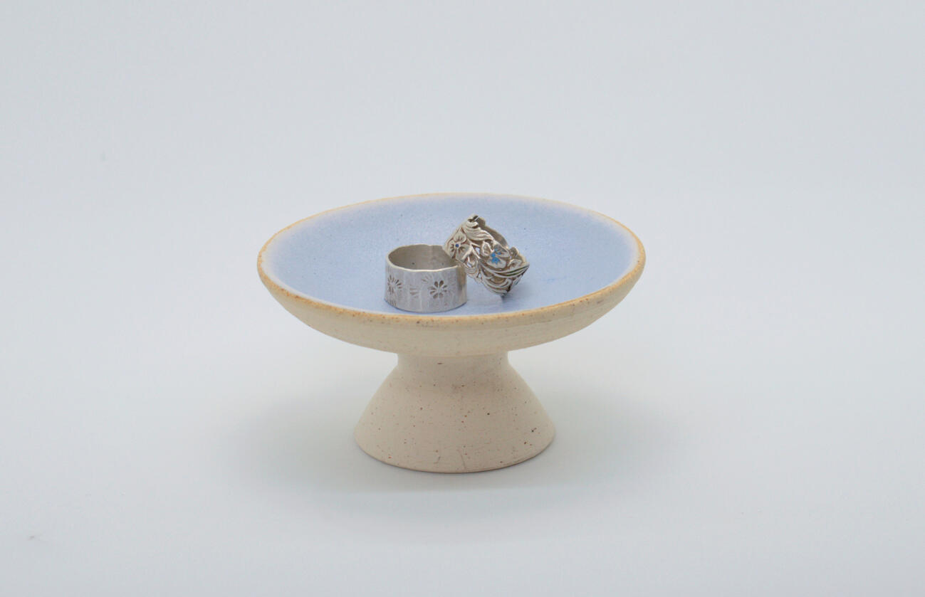 Small ceramic plate on elevated foot with rings resting on top.