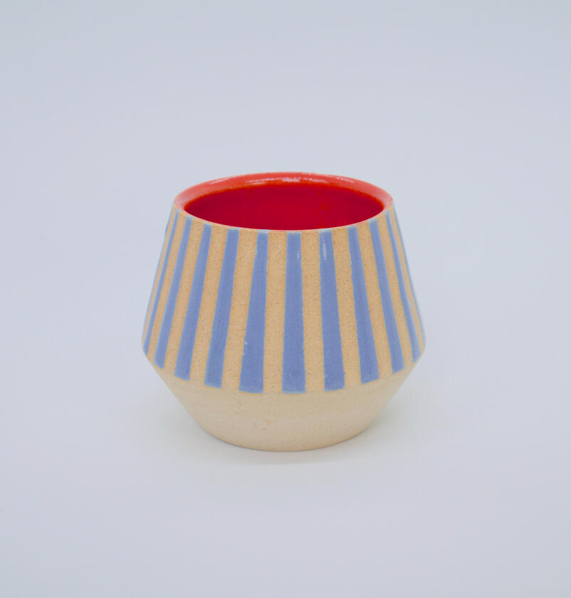 Ceramic cup with blue stripes on exterior and plain red interior.