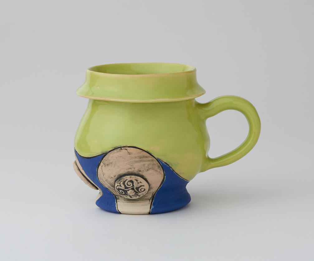 Green and blue mug with circular embossing along bottom edge.